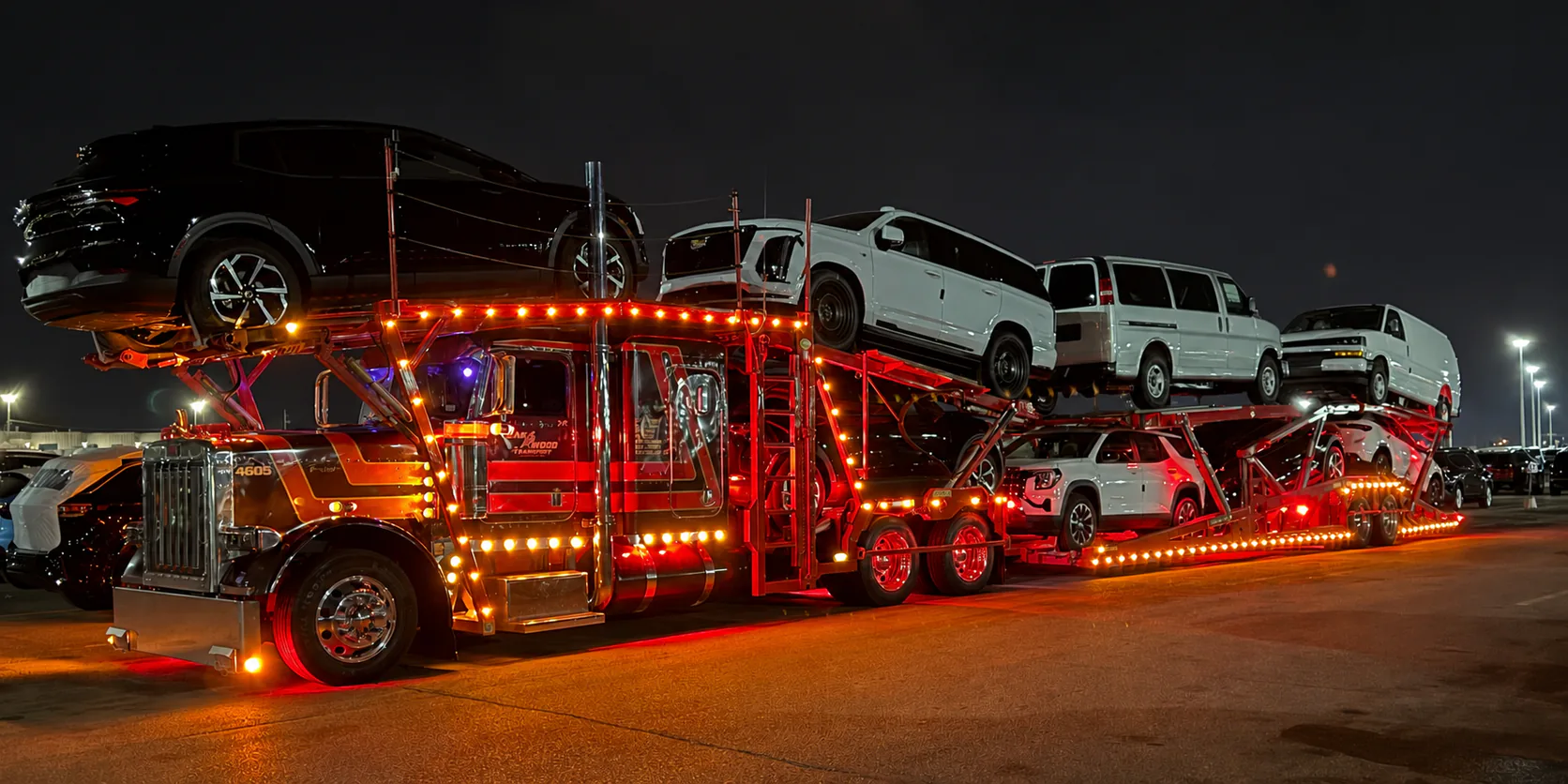 Illuminated Oakwood vehicle carrier loaded with vehicles at night.